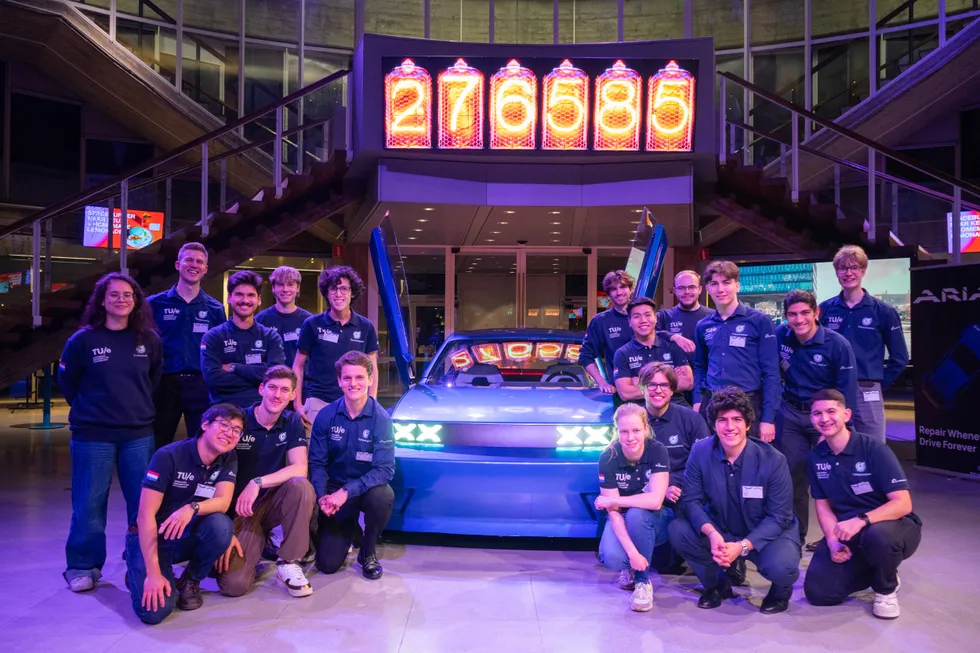Eighteen college students posing around a modular electric vehicle inside a museum.