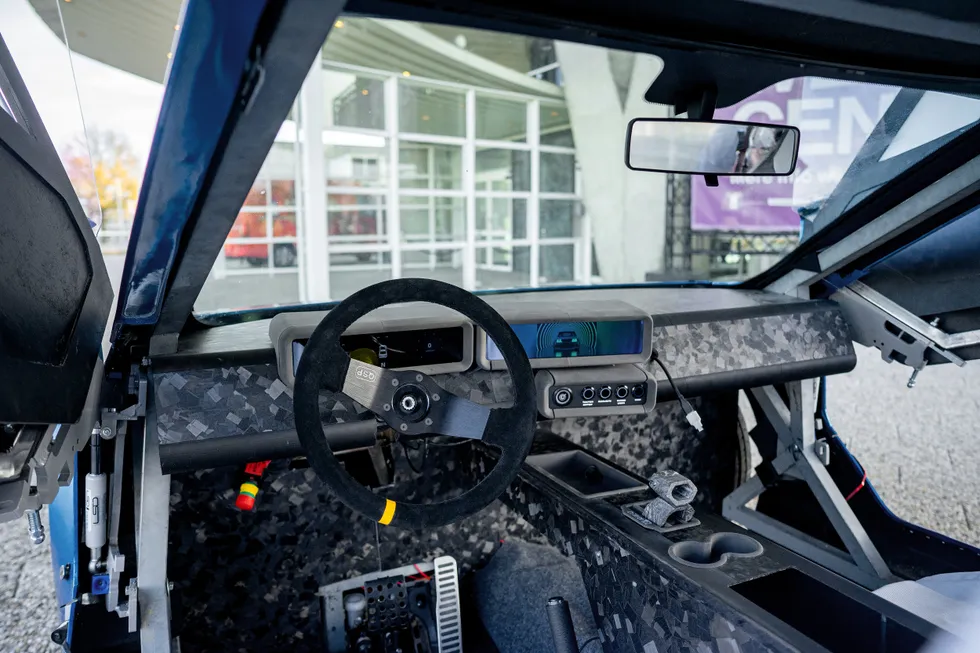 Interior view of the driver's side of a modular electric vehicle. Its elements are minimal and stripped down to essentials.