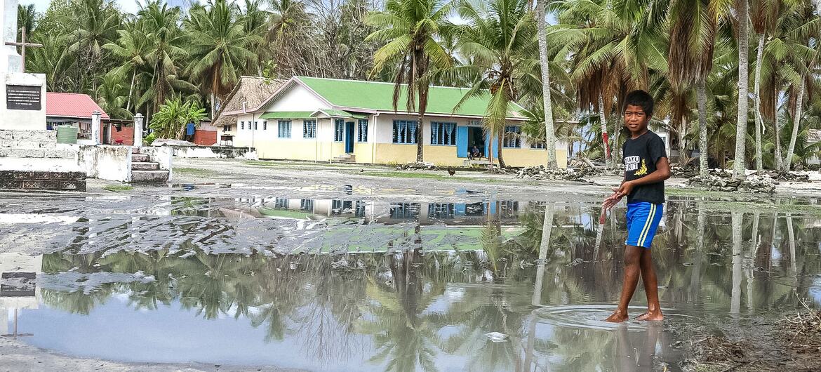A young Pacific Islander boy wades through floodwater in the main square of Nui Island, Tuvalu, over a month after Cyclone Pam caused widespread destruction and coastal erosion.