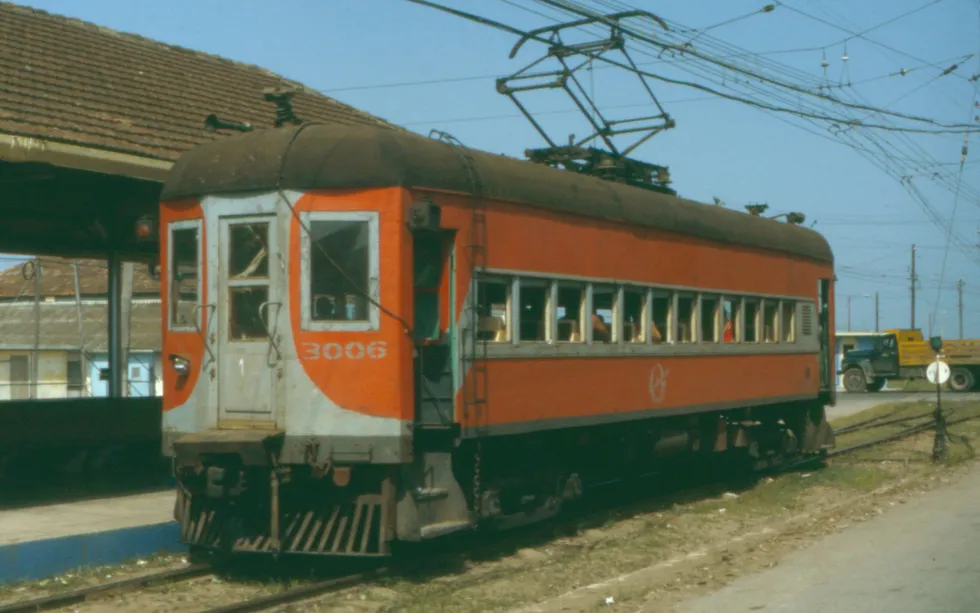 An old red electric passenger train car sitting on the tracks.