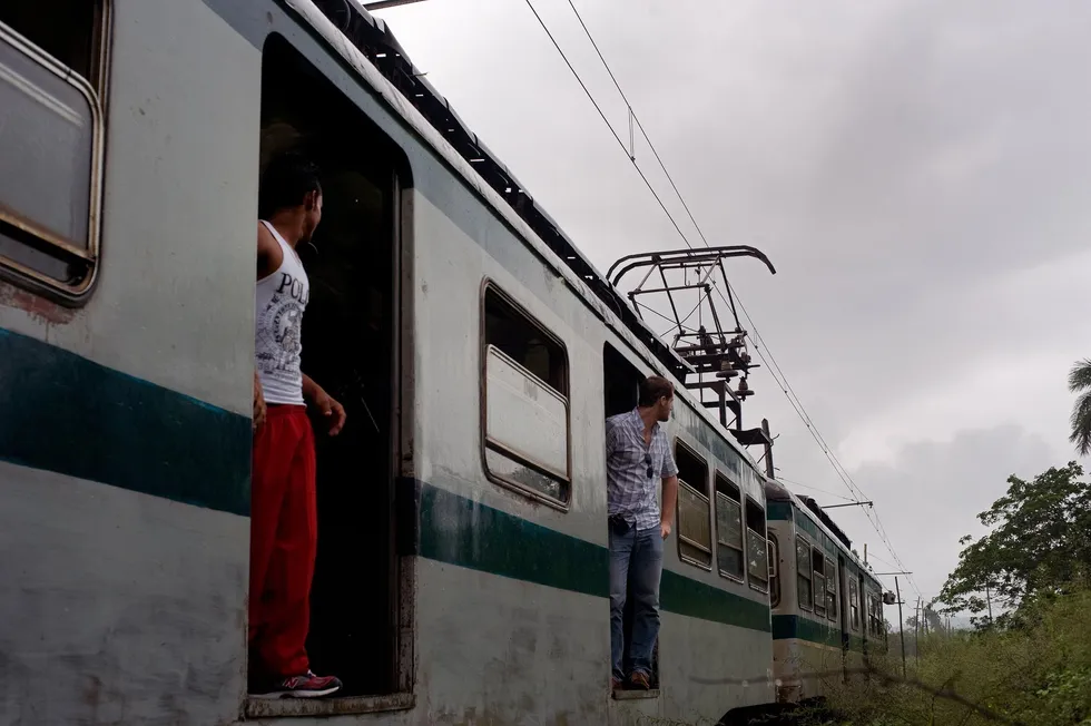 Photo of a stopped train, with passengers standing in the doorways looking down the track.