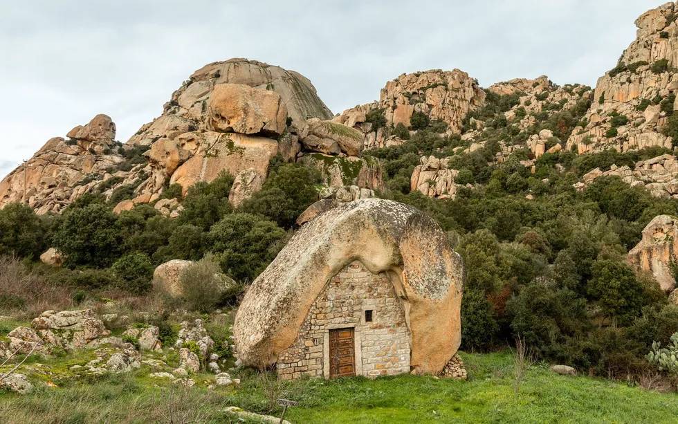 A hut with a rounded slab of rock as a roof and cut stone as walls, and a wooden door. 