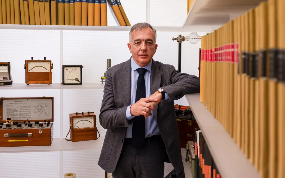 Man in a suit leaning on a bookshelf in an office.
