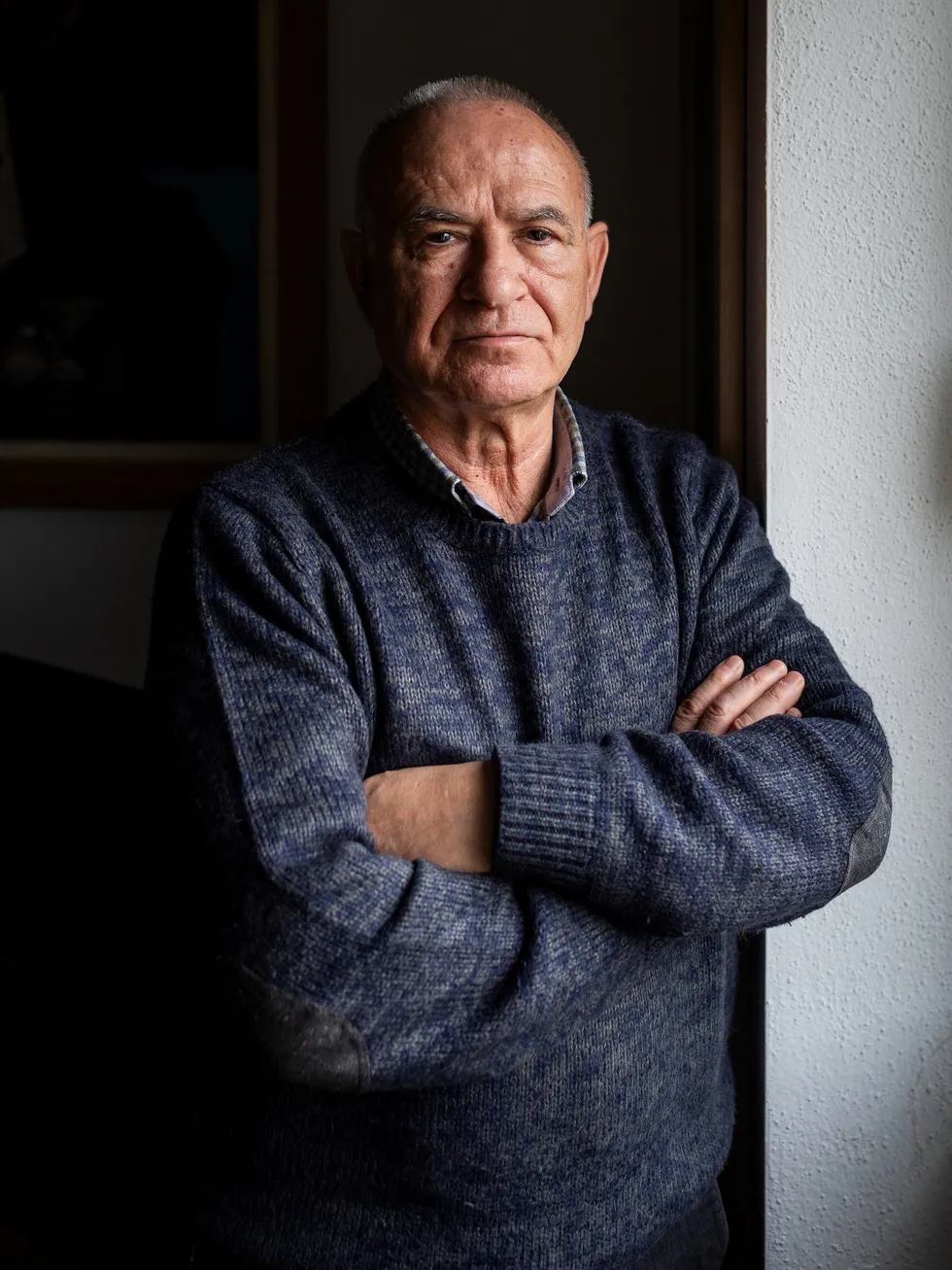 Man in a sweater and collared shirt leaning against a wall