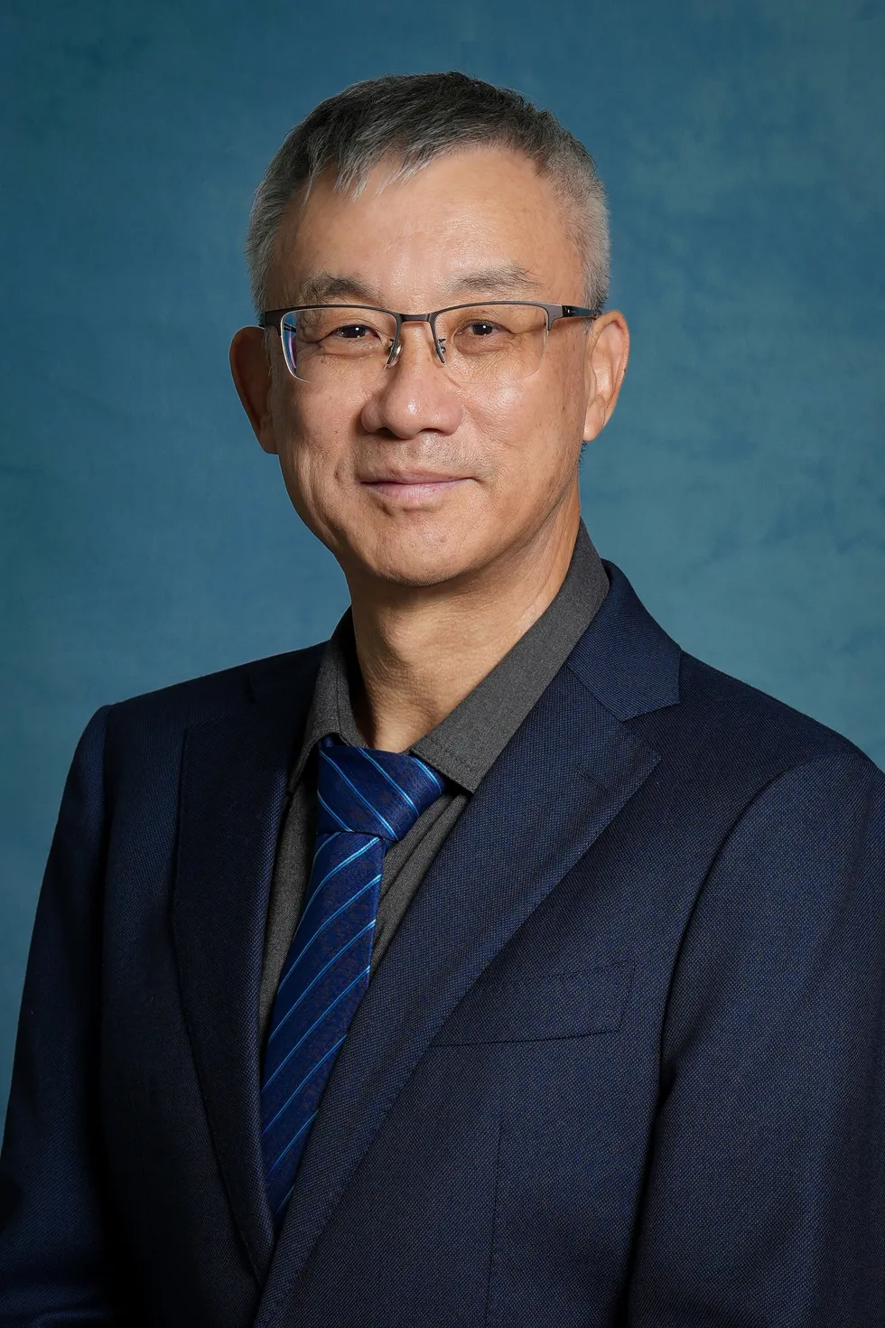 Person in navy suit and blue striped tie against a blue studio backdrop