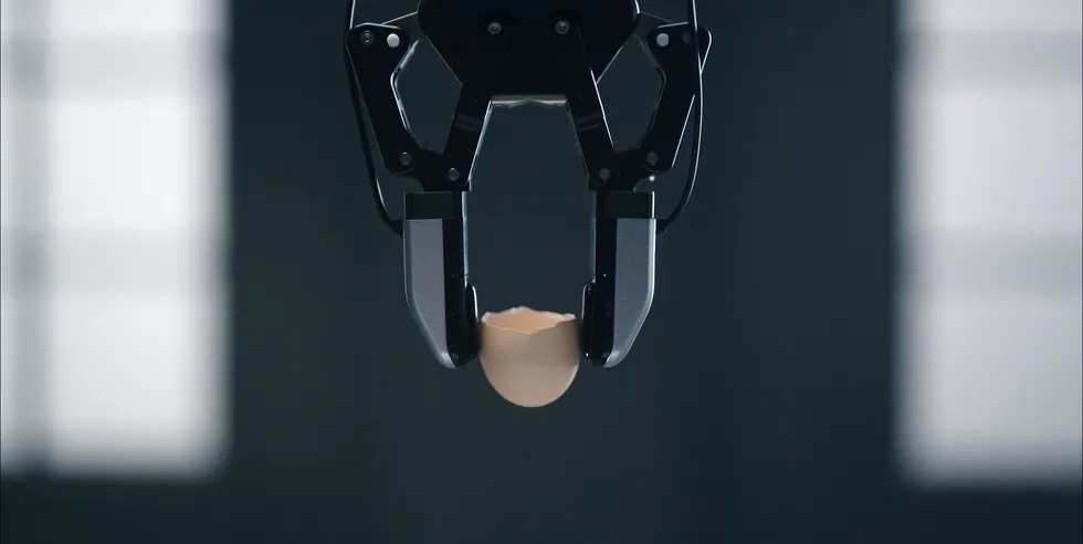 Robotic gripper delicately holding a cracked eggshell in a dimly lit room