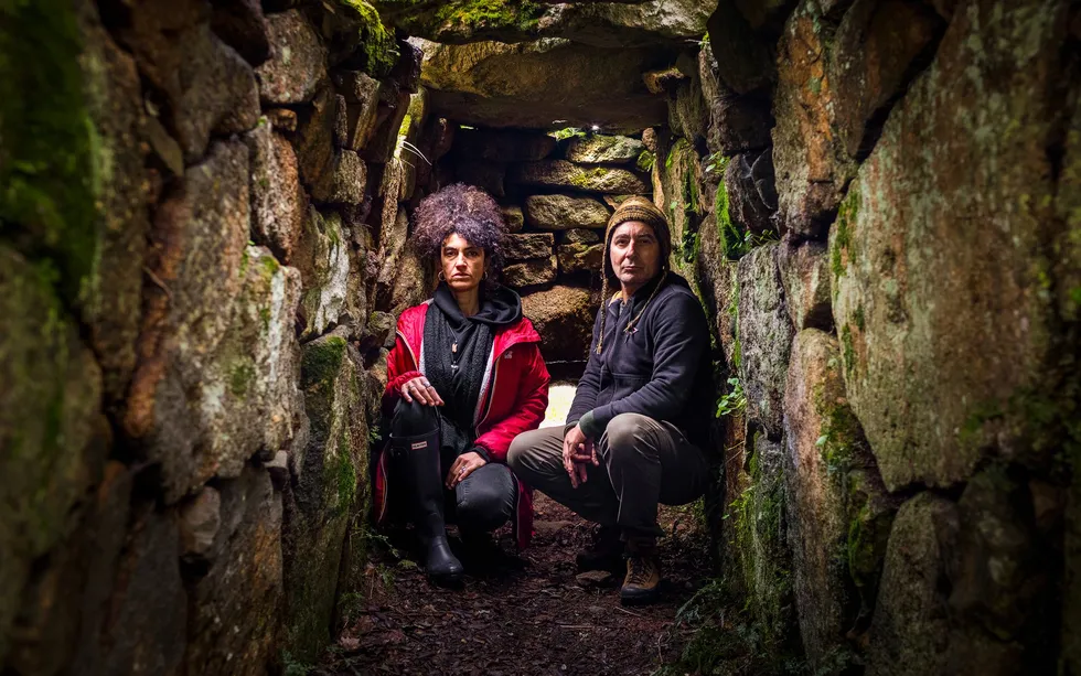 Woman and man sitting on stone steps, surrounded by moss-covered stone walls 