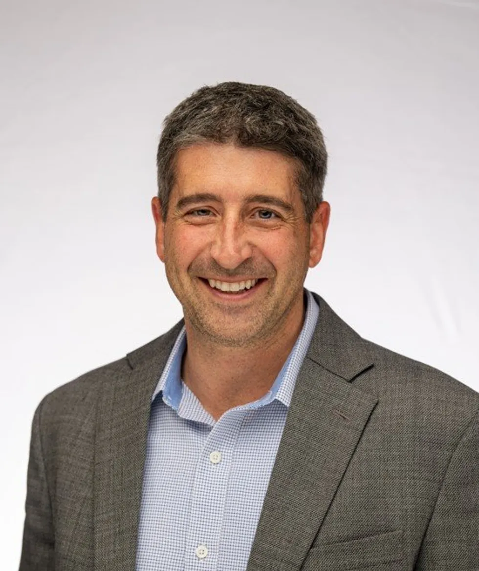 Man in gray blazer and blue shirt posed against a plain white background.
