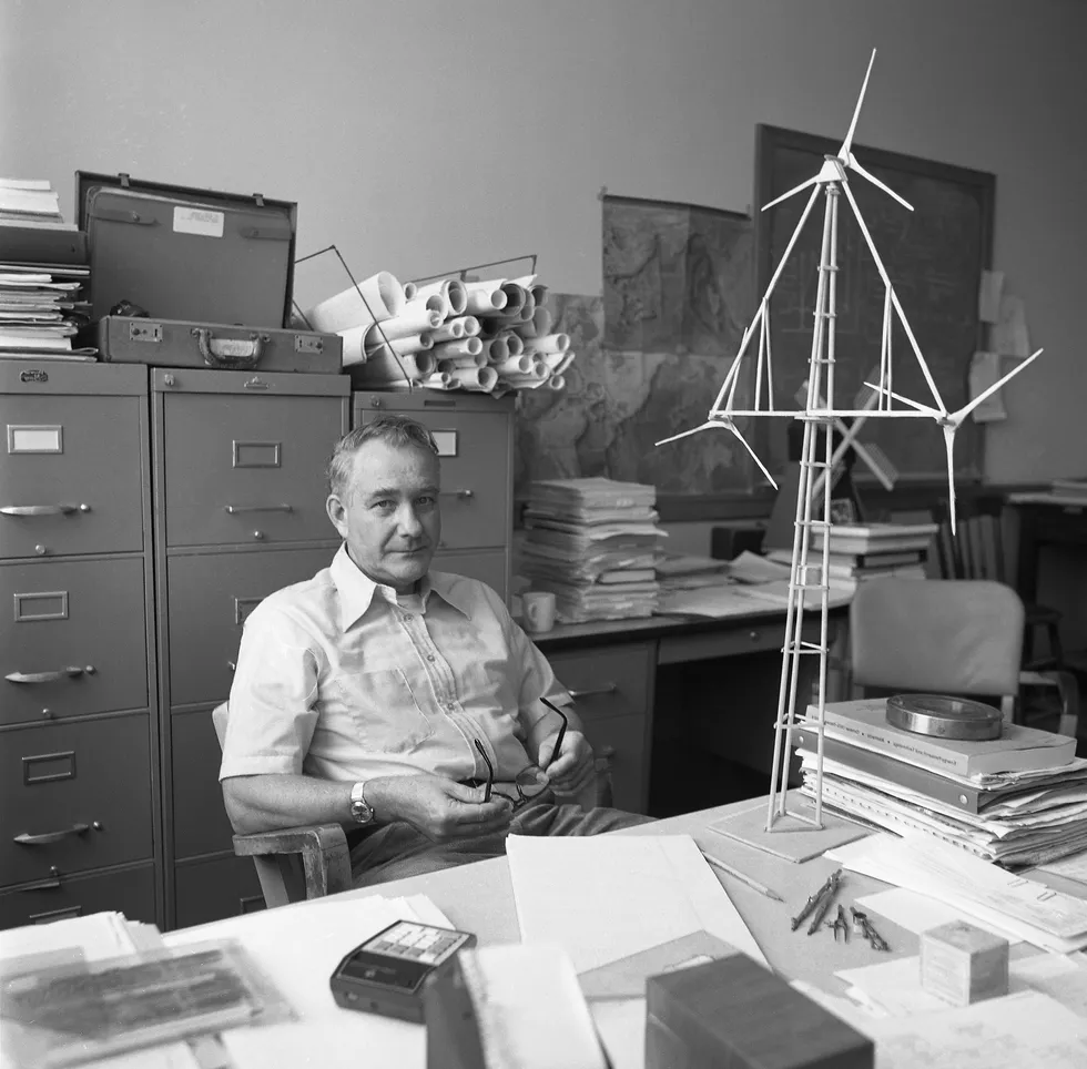 Man sits in a chair at his desk, leaning back and holding his eye glasses 