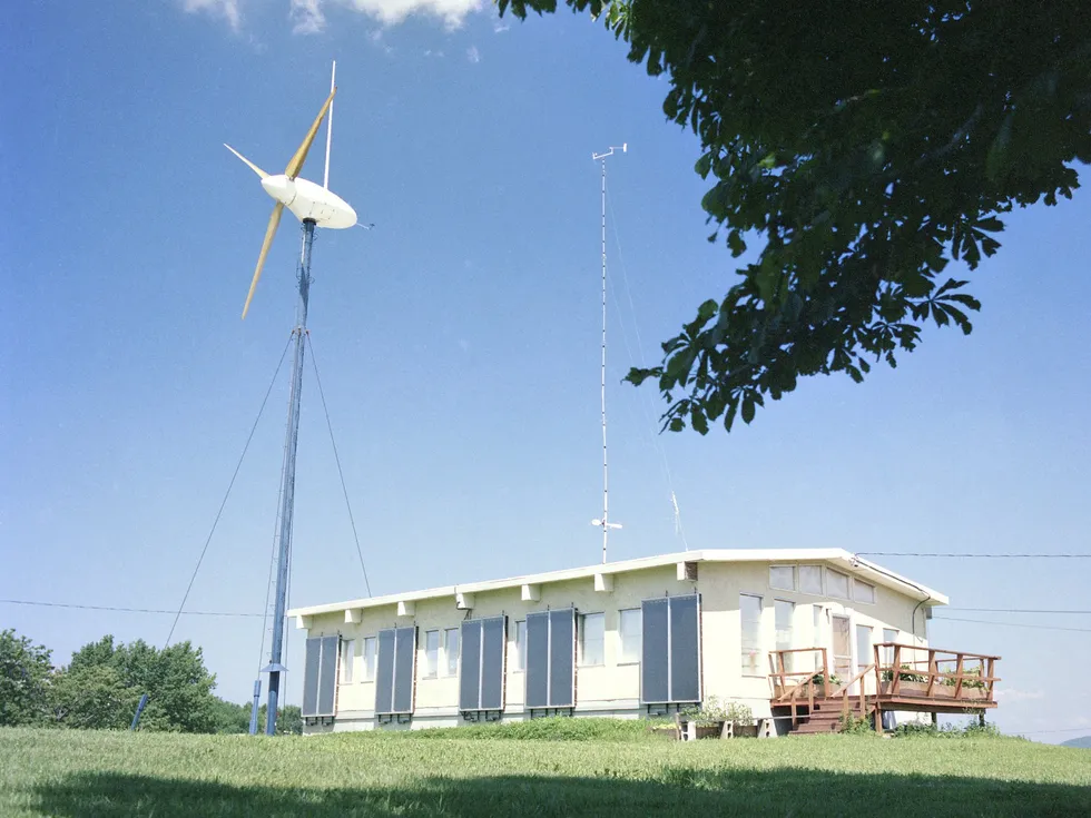 Modular home and wind turbine on a grassy hill on a sunny day 