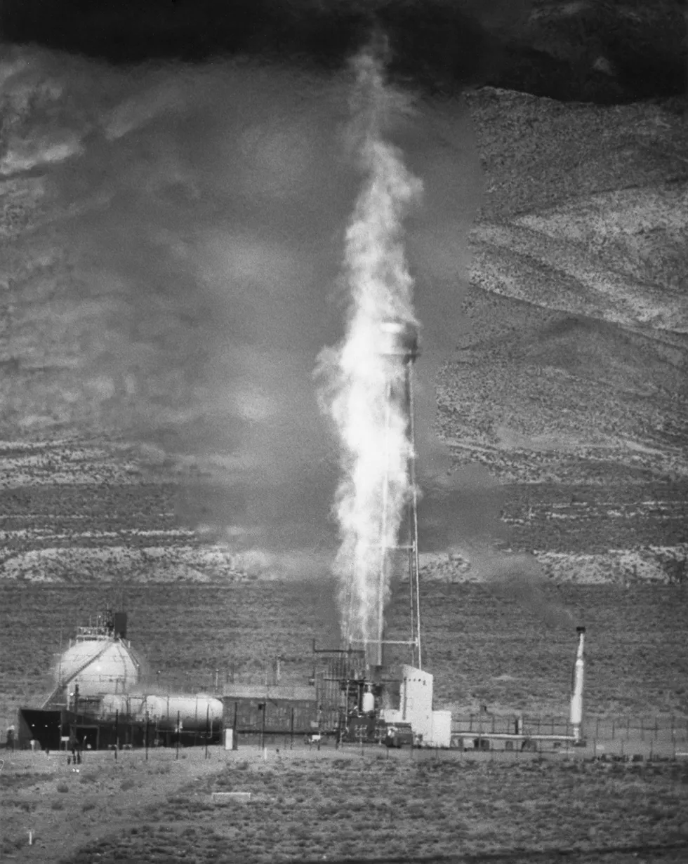 A photograph of a tall plume of rocker exhaust firing up into the air from a test stand in the desert.