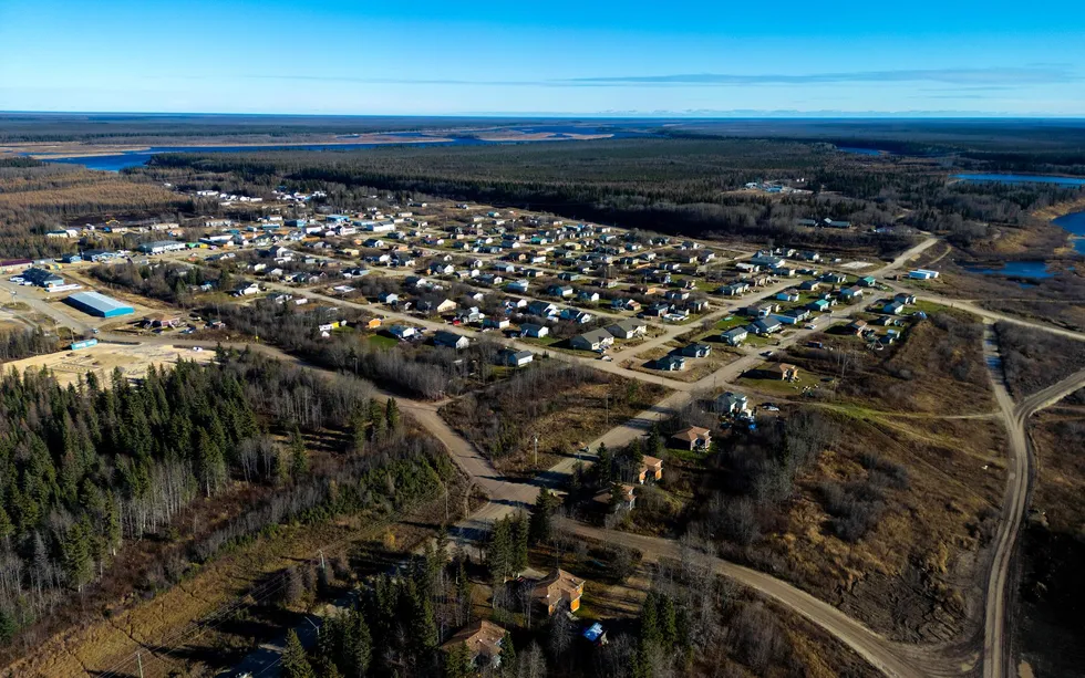 An aerial photo shows a grid of residential streets surrounded by forest. 