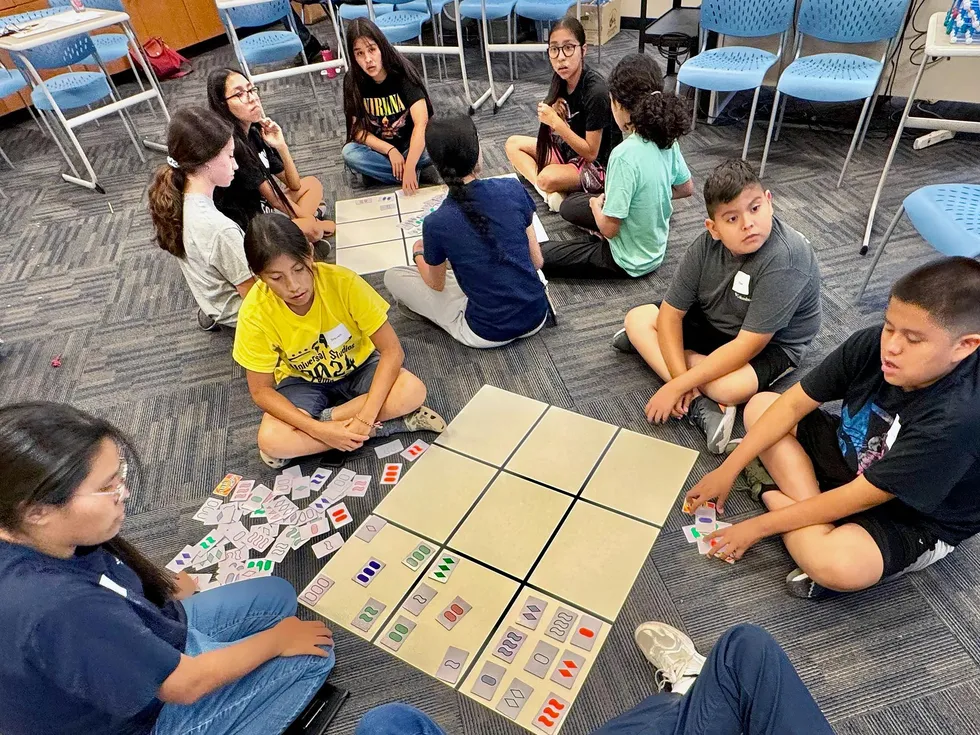 Native American middle school students sitting on a classroom floor while solving a mathematical pattern-matching game together.