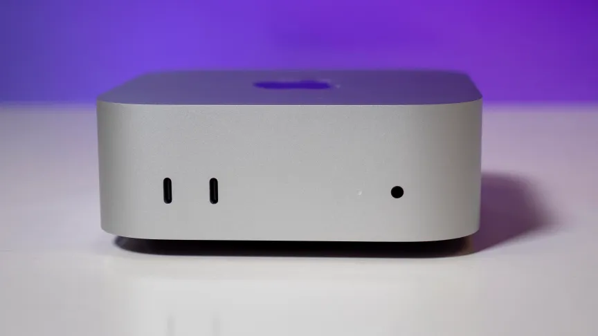 the front view of an apple mac mini sitting on a glossy white table in front of a purple background. 