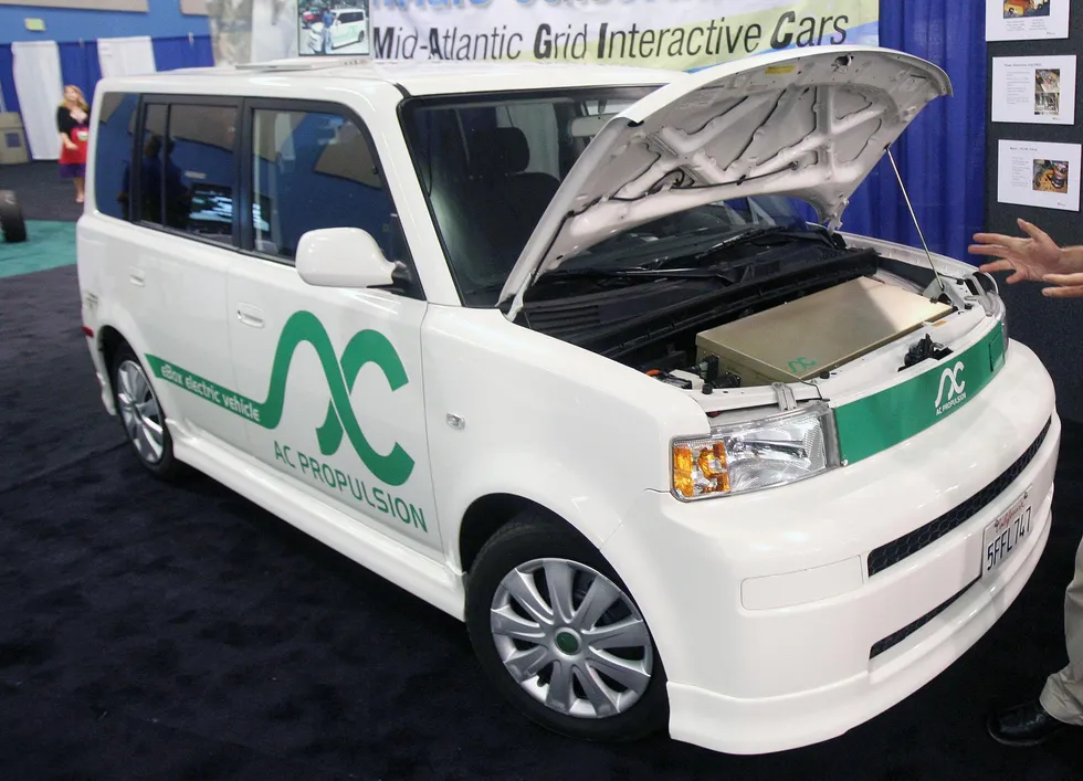 A boxy white vehicle is seen with its front hood raised.