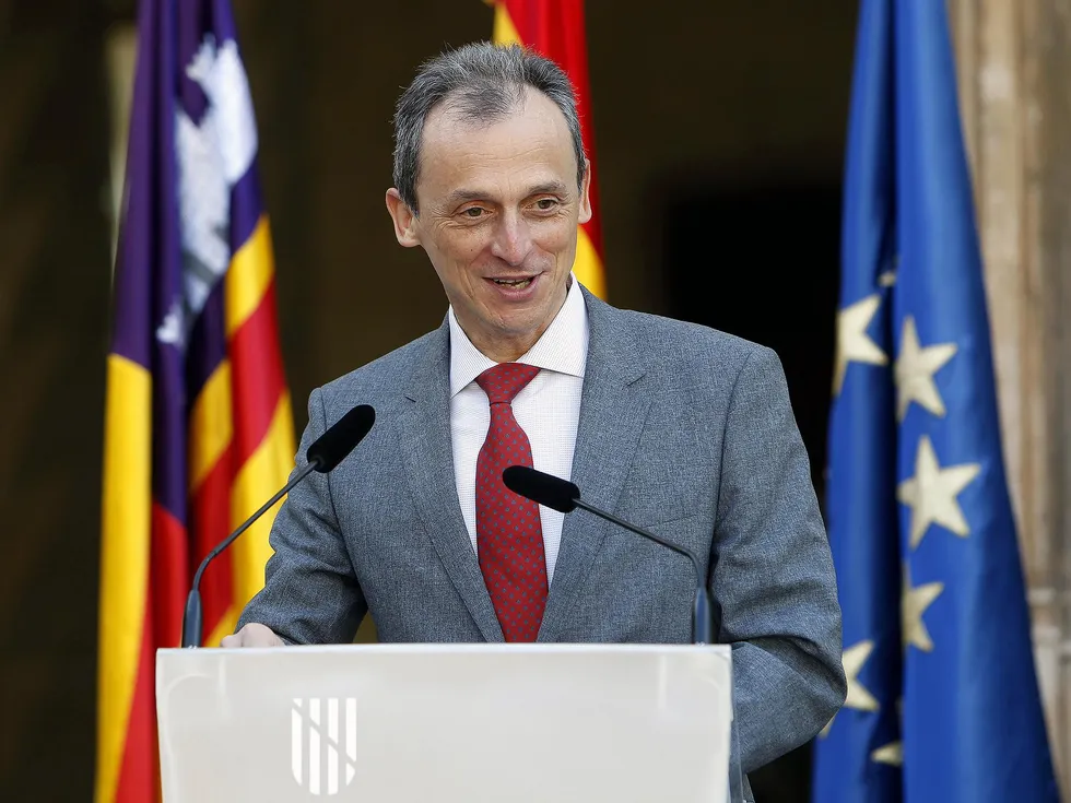 A middle-aged man in a suit and tie speaking behind a podium, against a backdrop with flags for the European Union, Palma de Mallorca and Spain.