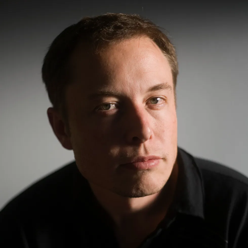 A portrait of a smug-looking man with thinning hair, lit from the side, and wearing a black shirt.