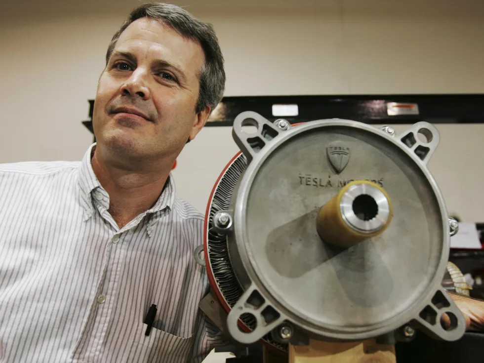 A smiling man in a striped shirt stands next to an electric motor.