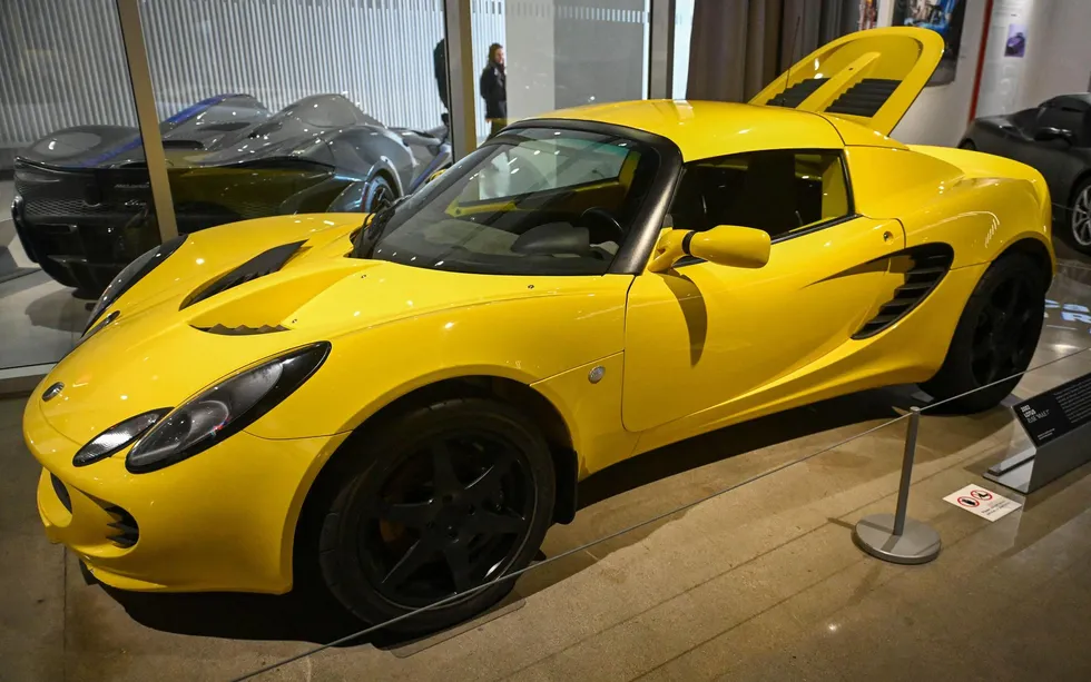 A yellow roadster is displayed in a museum setting.