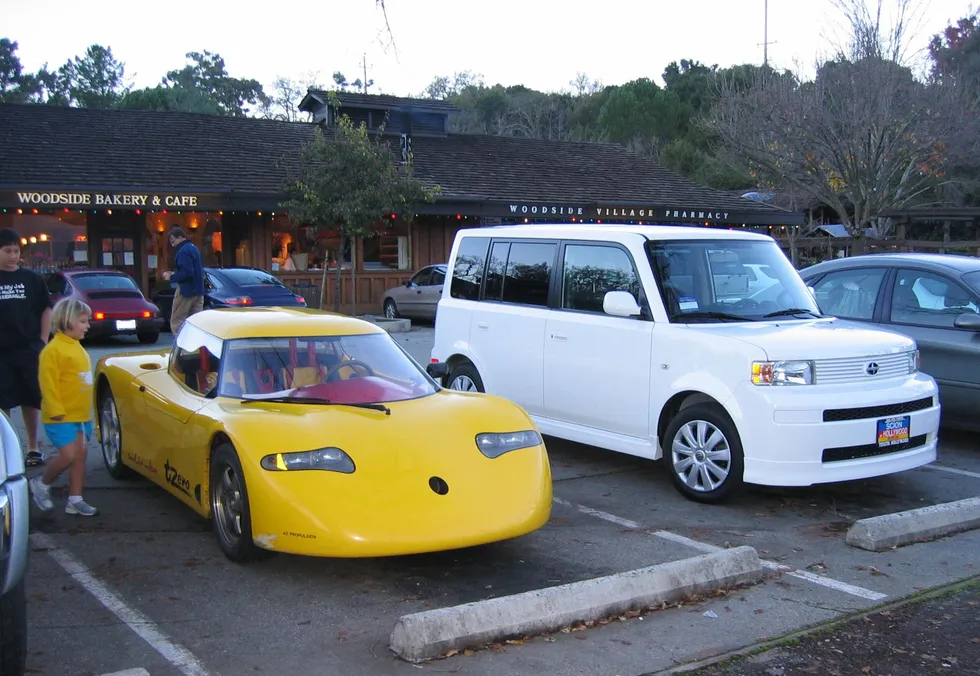 A yellow sports car is parked in a restaurant parking lot next to a boxy white vanlike vehicle.