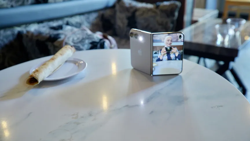 The iPhone Duo on a table, with the cover screen showing a preview of an image of a woman with a mug in hand.